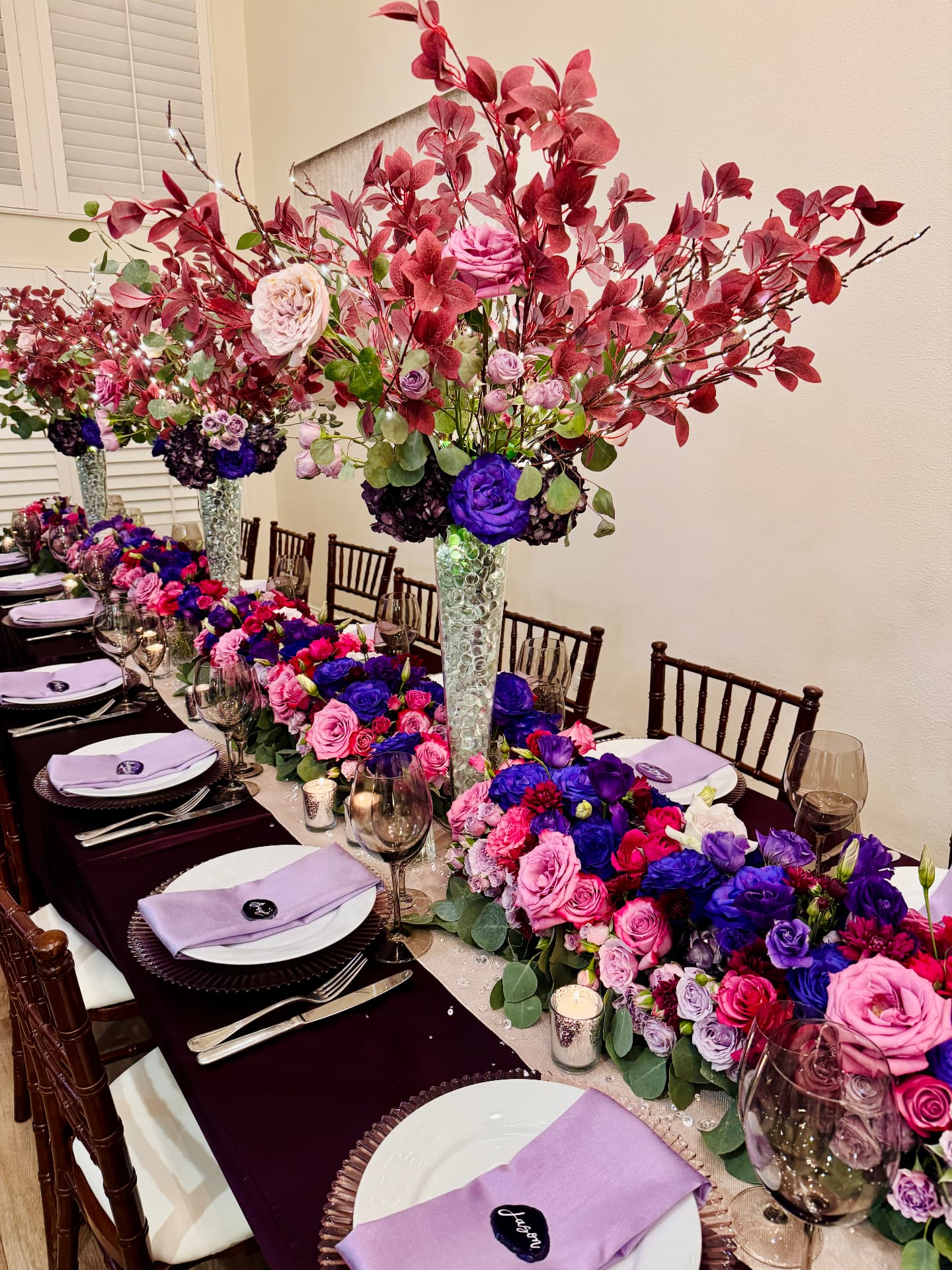 Long plum table with towering berry-toned centerpieces and a jewel rose runner