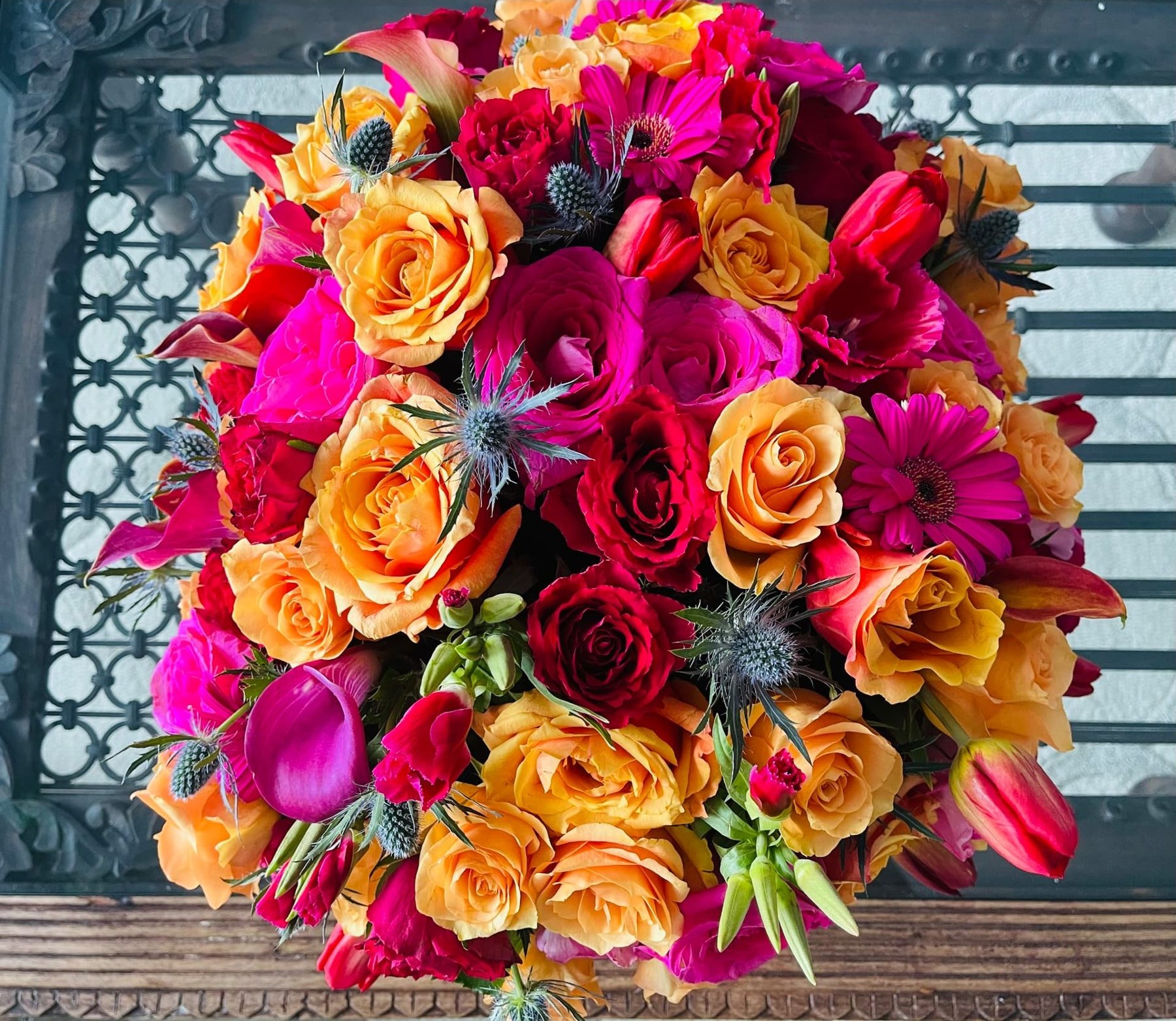 A saturated orange and magenta rose, tulip and thistle arrangement