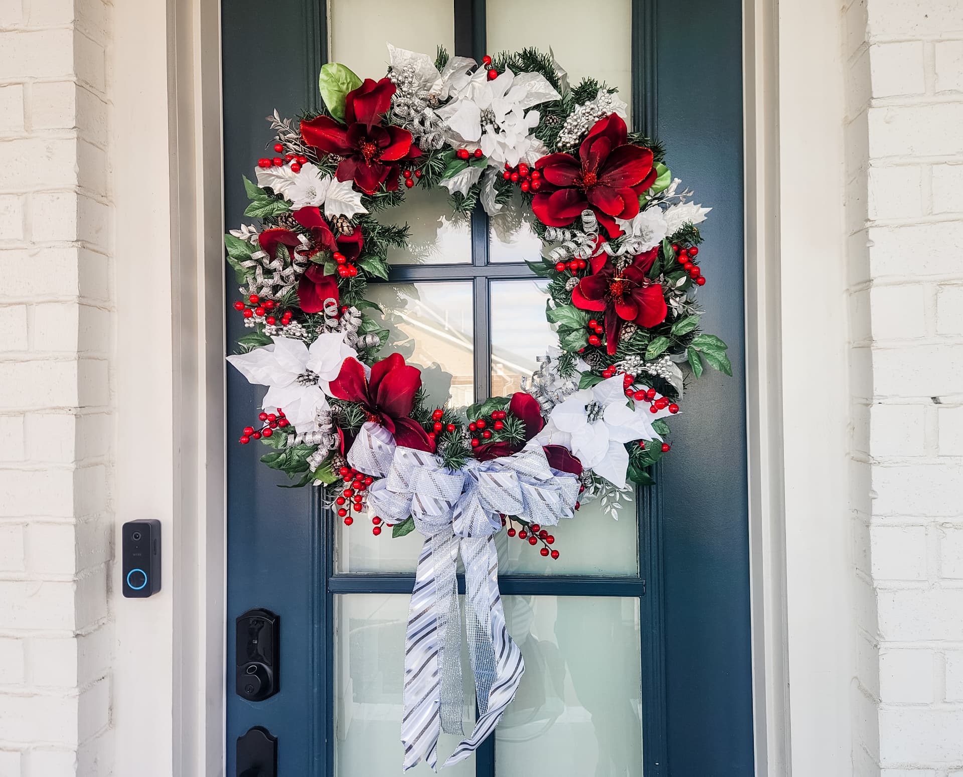 Crimson magnolia and white poinsettia wreath on a deep teal front door